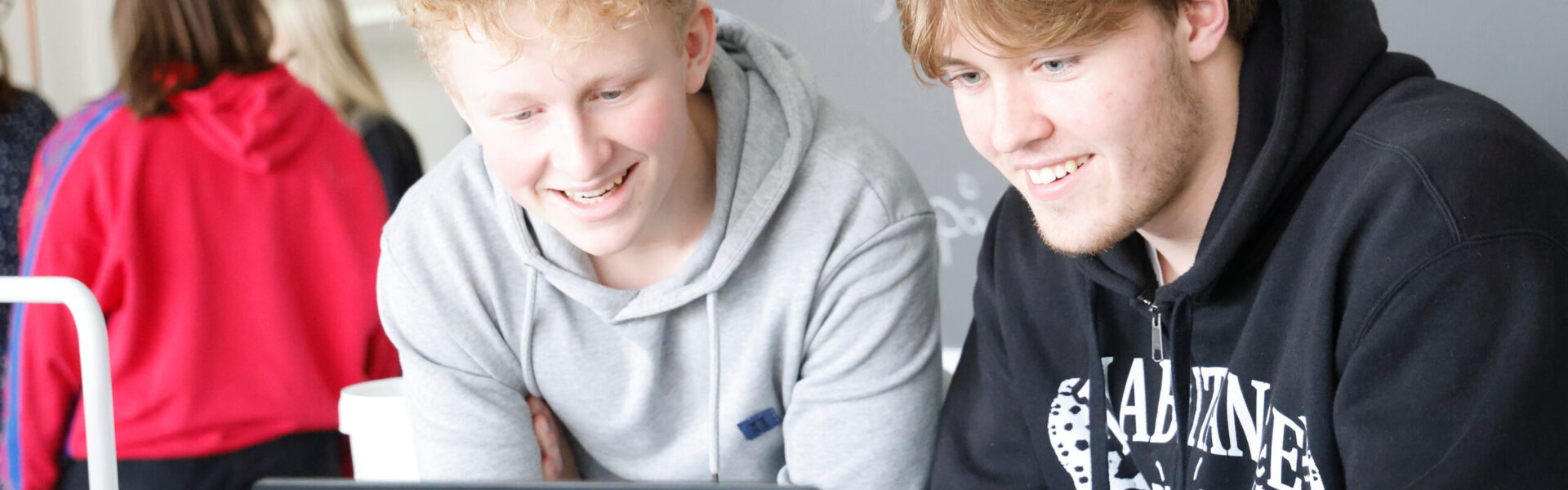 To drenge sidder i klasselokale og kigger på en computer
