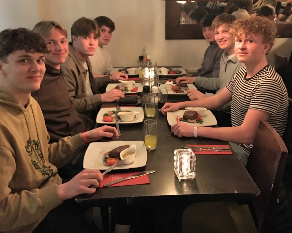 På studietur i Europa. Syv drenge sidder klar til at spise på restaurant.