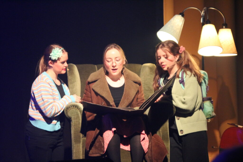 Livsbilleder. Tre elever på scenen. En spiller en ældre dame i en lænestol, der fortæller sine to børnebørn om hendes barndom.