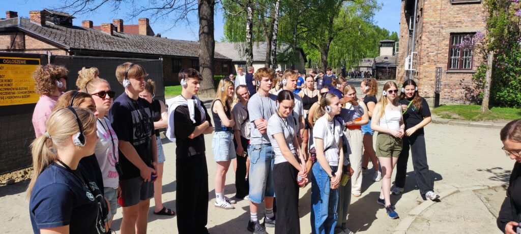 Eleverne besøger Auschwitz-Birkenau, som en del af deres tur til Krakow. De står i solskin og lytter til guidet rundvisning.